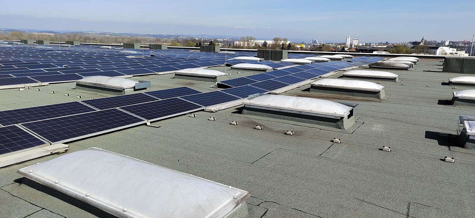 Cupole luminoase pe un acoperiș industrial plat, lângă panouri fotovoltaice